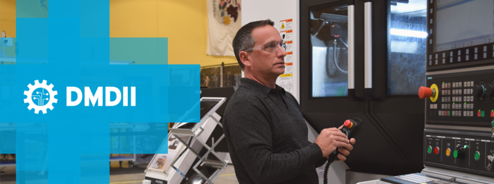 A man in safety goggles adjusts the controls on a digital machine tool, with the DMDII logo on the side.